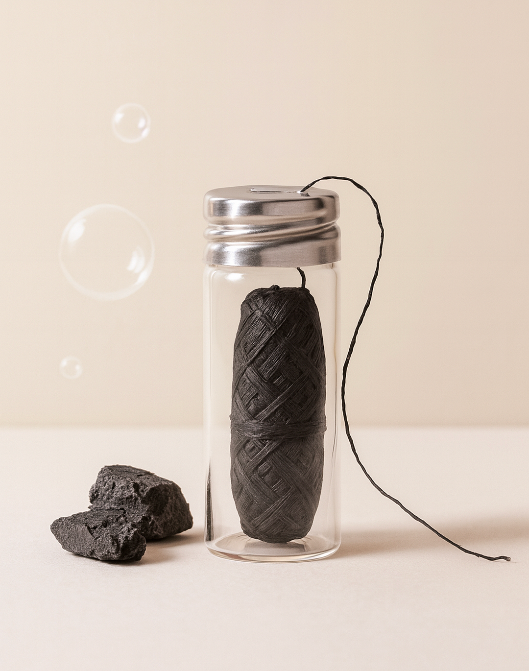 Fil dentaire noir au charbon actif dans un flacon en verre, brin déroulé, morceaux de charbon et bulles