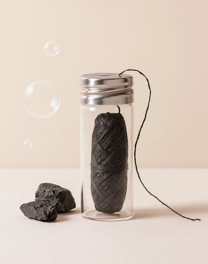 Fil dentaire noir au charbon actif dans un flacon en verre, brin déroulé, morceaux de charbon et bulles
